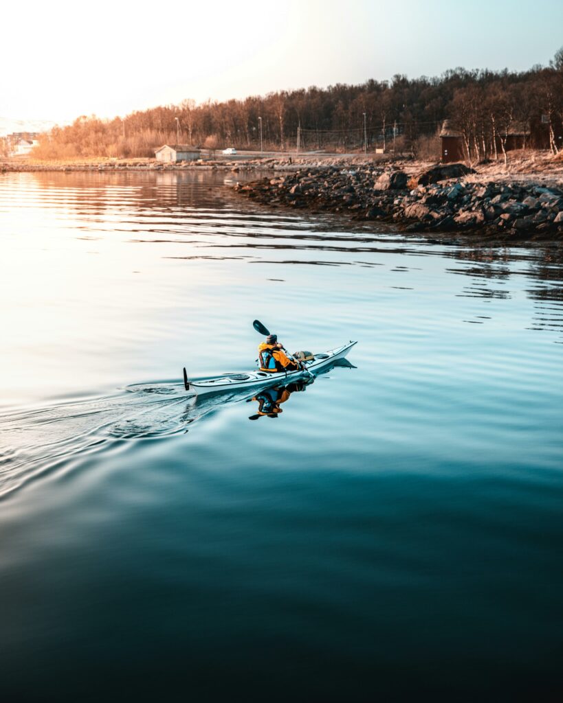 Kayaker paddles across calm waters near a rocky shoreline, perfect for a tranquil outdoor adventure.