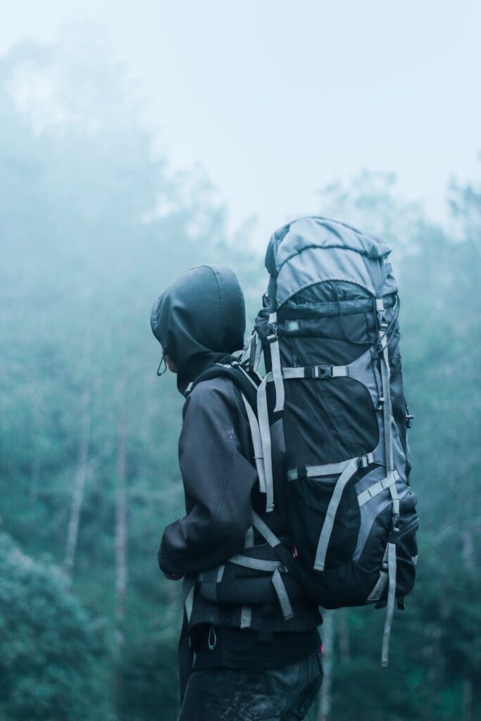 Solo hiker with large backpack in a misty forest, exploring nature's serene beauty.