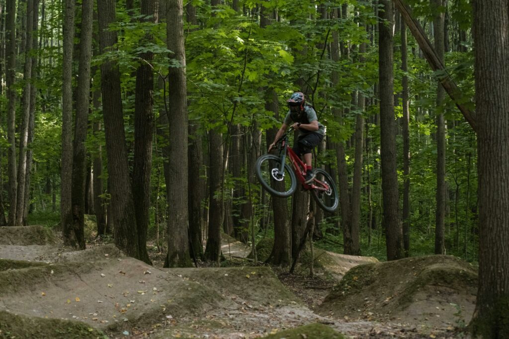 Cyclist performing an aerial BMX stunt in a dense forest track.