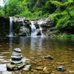Peaceful forest waterfall with serene stone cairn, ideal for nature and travel themes.